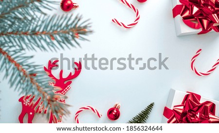 Holiday winter red. White gift box with scarlet ribbon, New Year balls, candy and winter tree in Christmas composition on white background for greeting card. Festive decoration, copy space.