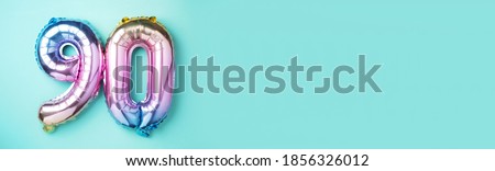 Rainbow foil balloon number, digit ninety. Birthday greeting card with inscription 90. Anniversary concept. Top view. Colored numeral on blue background. Numerical digit, Celebration event, template.