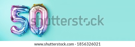 Rainbow foil balloon number, digit fifty. Birthday greeting card with inscription 50. Anniversary concept. Top view. Colored numeral on blue background. Numerical digit, Celebration event, template. Royalty-Free Stock Photo #1856326021