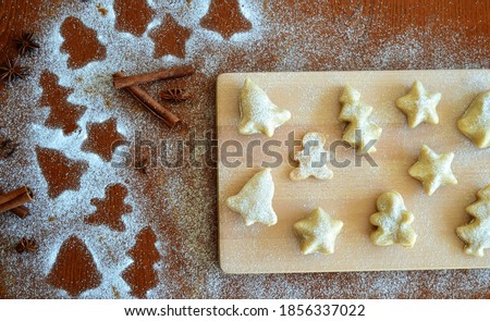 Line of Christmas silhouettes with gingerbread man, bells, Christmas trees and stars on a wooden background with powdered sugar  and cinnamon sticks, star anise and cloves and a cookies next to it