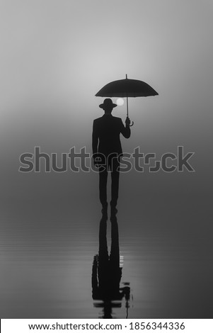 surreal portrait of a man in a suit and hat with an umbrella standing on the water at sunrise on a foggy morning
