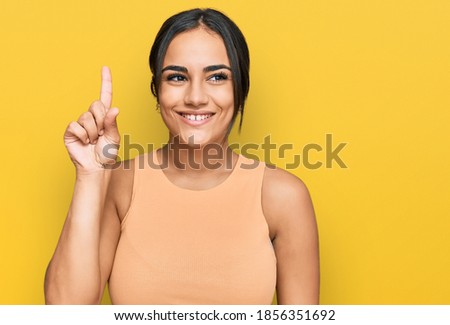 Young brunette woman wearing casual clothes showing and pointing up with finger number one while smiling confident and happy. 