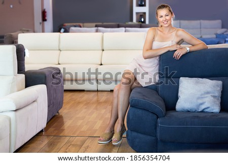 Adult glad cheerful positive female touching sofa in the furniture store before the buying.