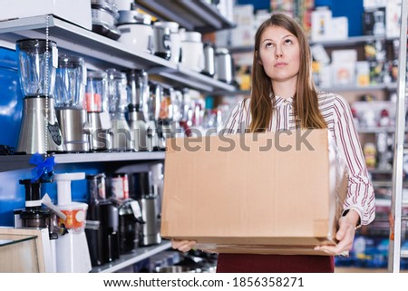 Thoughtful girl holding cardboard box with purchase in a store of house appliances