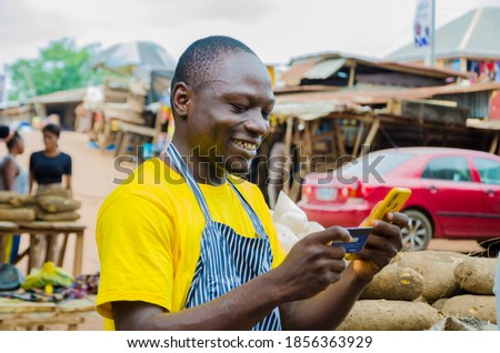 young handsome african trader smiles as he uses his phone and credit card.