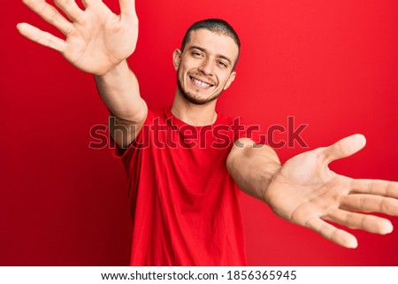 Young hispanic man wearing casual red t shirt smiling cheerful pointing with hand and finger up to the side 