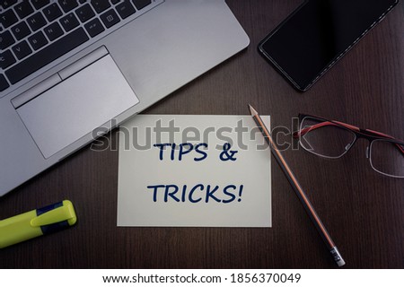 Tips and tricks card. Top view of office table desktop background with laptop, phone, glasses and pencil with card with inscription tips & tricks.  Business concept.