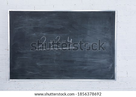 White brick wall. It's written in white chalk on a blackboard - two plus two equals four. The basics of arithmetic start with the youngest grades in every school in the world.