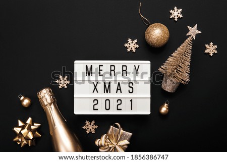 Lightbox with text MERRY XMAS 2021 and golden christmas decor on black background. Creative layout in monochrome colors.