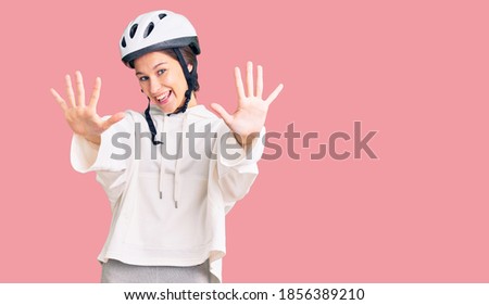 Beautiful brunette young woman wearing bike helmet and sporty clothes showing and pointing up with fingers number ten while smiling confident and happy. 