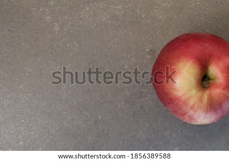 A top view closeup of a big juicy red apple placed on a grey surface
