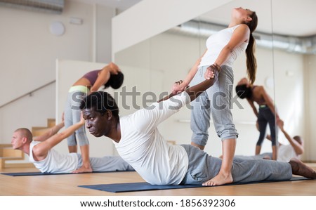 Young men and women maintaining healthy lifestyle practicing partner yoga at group lesson
