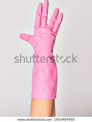 Hand of caucasian young woman wearing pink cleaning glove doing salutation over isolated white background