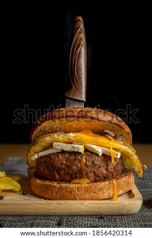 A vertical closeup shot of fresh tasty homemade beef burger with a knife on a wooden tray
