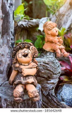 Smiley clay doll girl on wood in the park, funny traditional Thai garden sculpture