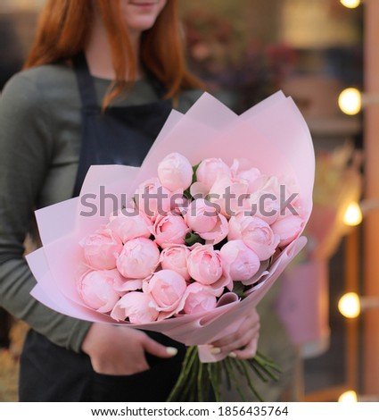 Young woman florist holding big beautiful blossoming mono bouquet of pink peony flowers.