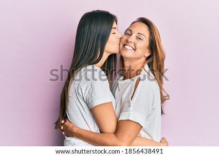 Beautiful hispanic mother and daughter smiling happy hugging and kisisng over isolated pink background.