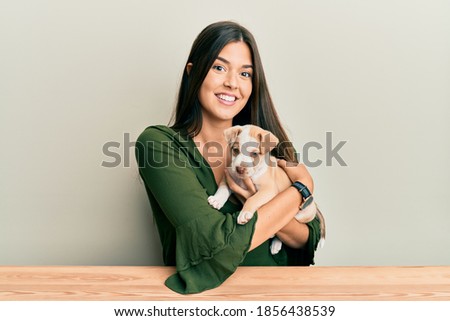 Young hispanic girl smiling happy and hugging dog sitting on the table over isolated white background.