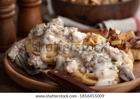 Closeup of biscuits with creamy sausage gravy and fried potatoes on a wooden plate Royalty-Free Stock Photo #1856455009