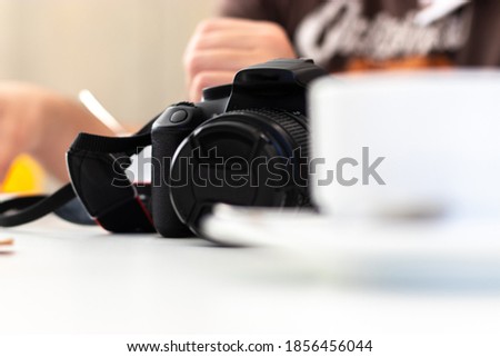 Older entry level dslr camera standing on the table, bright white coffee mug in the foreground. Photographer taking a break and relaxing, leaving his camera on the table