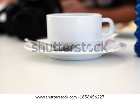 White wide ceramic old fashioned coffee mug standing a white plate with a metal spoon on it