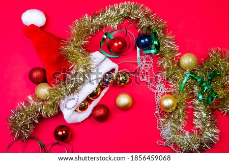 Close up of christmas decorations around a santa hat, baubles and tinsels. Glimmering and festive. Studio photo on red background. Selective focus on subject.
