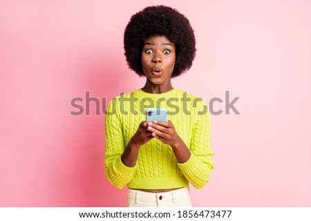 Photo portrait of shocked girl holding phone in two hands isolated on pastel pink colored background