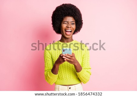 Photo portrait of winking girl with open mouth holding phone in two hands isolated on pastel pink colored background