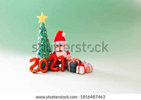 Playful clay christmas concept. Colorful handmade miniature Christmas tree, presents and Santa Claus with mask on green background. 2021 new year.