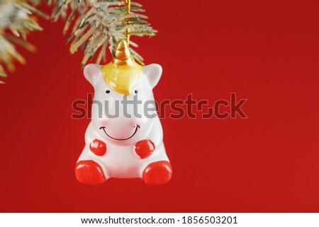 Unicorn figurine on a Christmas tree on a red background, free space for text.