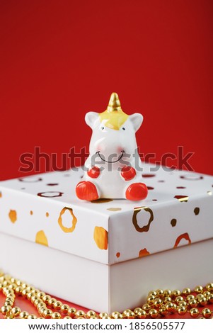 Unicorn figurine on a gift box with gold beads on a red background with free space.