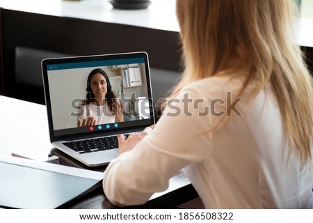 Rear back view young woman holding video call conversation with female colleague in wireless headphones, discussing working issues remotely or taking educational online class, self-isolation concept. Royalty-Free Stock Photo #1856508322