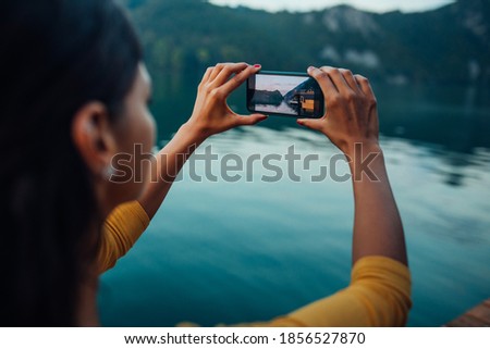 Young woman sitting near a river and taking photo by phone