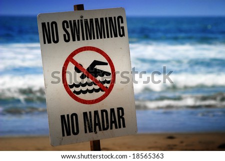 no swimming sign on a beach with waves in the background