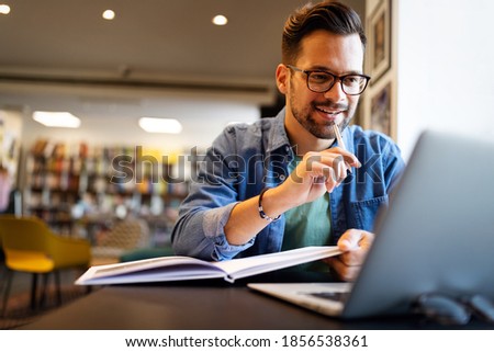 Smiling male student working and studying in a library Royalty-Free Stock Photo #1856538361