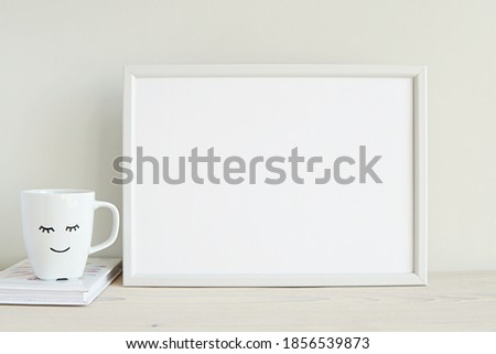 Blank white frame mockup for artwork display, cup with smile, white interior.	