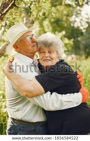 Adult couple in a summer garden. Handsome senior in a white shirt. Woman in a black blouse.