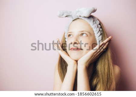 Face of beautiful, happy, positive teenage girl with gray fluffy cosmetic bandage on her head on a tender pink background. Girl put her chin in her palms