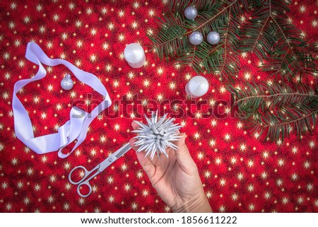 Christmas background with homemade 3D star.Hands of woman creating Christmas decoration.Xmas colorful background.Winter holiday seasonal decor.Making DIY project.Handcraft activity top view copy space