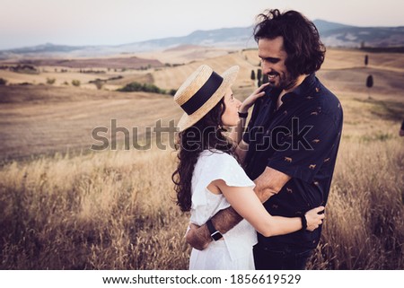 a boy and a girl hug each other as they look into each other's eyes in the middle of the summer countryside at sunset