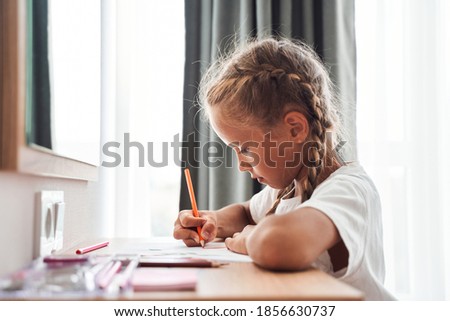 Happy little adorable pleasant child girl sitting at table and drawing at the bedroom. Stock photo