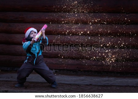 boy explodes a firecracker, holding it in his hand, with a Christmas dwarf hat on his head, standing against a dark background. Christmas and New year concept. Using a NASA image
