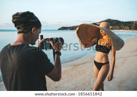 Photographer shooting model wearing bikini and big straw hat