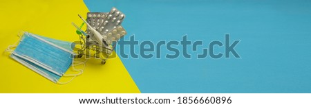 Purchase of medicines and masks. Pills, thermometer and syringe in a shopping cart. Top view, place for text on yellow and blue background
