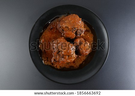 Ration of bullfighting oxtail stewed on black plate and black background