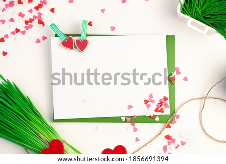 Two envelopes are connected with clothespins with hearts, a bouquet of wheat grass and many small hearts on a light background. Top view with space to copy. Concept of holiday backgrounds.