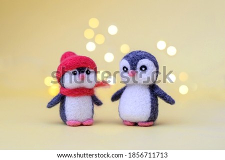 Two Christmas toy felted wool cute little penguins on a yellow background with bokeh