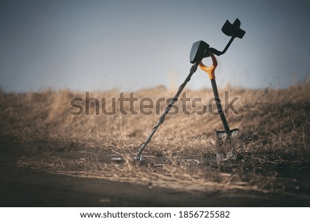 Metal detector with a spade on the old field background.