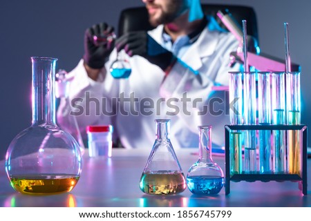 Doctor creates vaccine. Test tubes next to laboratory assistant. Doctor in background mixes liquid in test tubes. Medicine for virus is in lab glussware. He synthesizes vaccine. Vaccine test concept Royalty-Free Stock Photo #1856745799