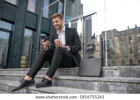 Social media. Elegant male businessman sitting on the steps and reading something online